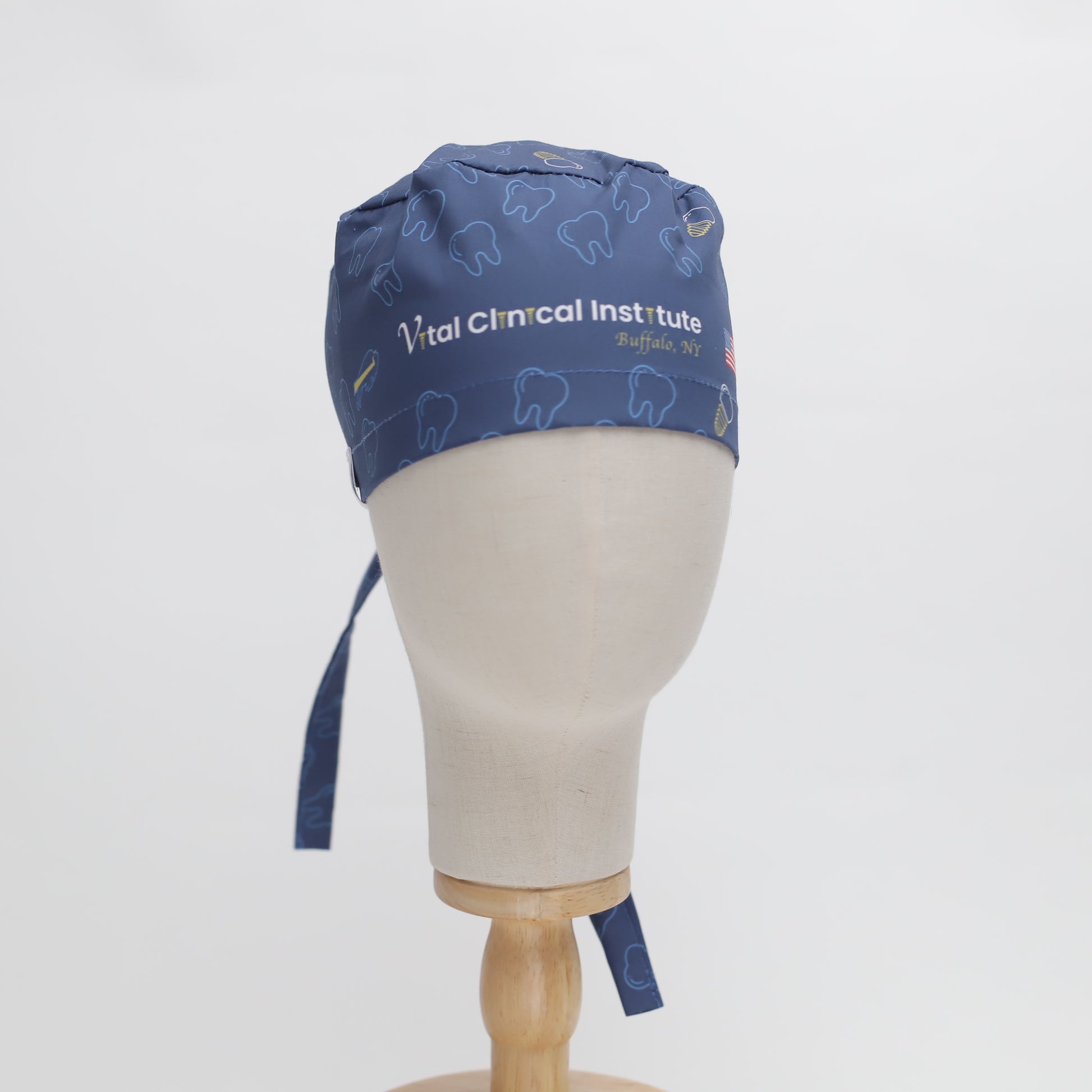 The mannequin head showcases a blue Medicus Scrub Caps specific custom printed placement scrub cap with teeth patterns and embroidered text, set against a white background.