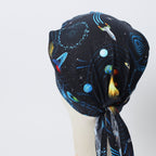 Side view of space-themed scrub cap with rockets, planets, and spaceships on dark starry background
