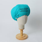 Turquoise scrub cap with black text displayed on mannequin head from side angle