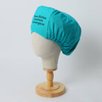 Teal turban-style scrub cap with black text embroidery shown on white mannequin head side view