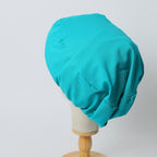 Turquoise turban-style scrub cap shown in side profile view on white mannequin head