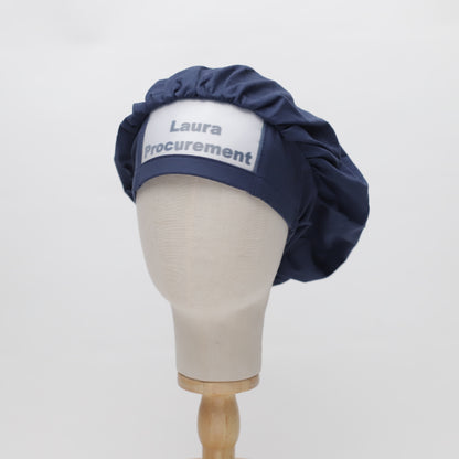 Mannequin head wearing a navy Medicus Scrub Cap with white embroidered text 'Laura Procurement.' Reusable and available in 22 colours.