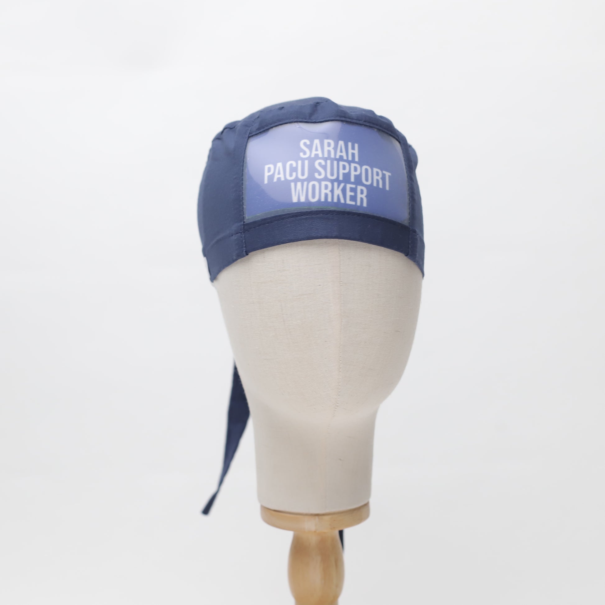 Displayed on a mannequin head, the ClearName navy scrub cap from Medicus Scrub Caps features a custom name patch and ties at the back.