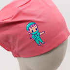 Close-up detail of pink scrub cap featuring cartoon surgeon character with teal scrubs and pink hair