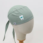 Sage green scrub cap with white tooth logo detail, side profile view on mannequin head