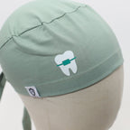 Close-up detail of sage green scrub cap featuring white tooth with green braces vinyl design