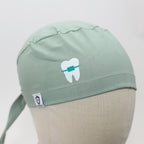 Close-up view of sage green scrub cap featuring white tooth with teal braces design