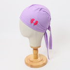 Purple scrub cap with red kidney bean design shown from side angle on wooden mannequin head