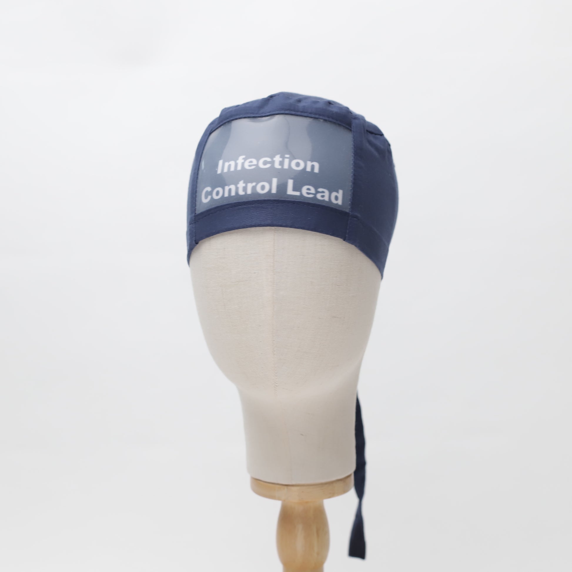 A mannequin head displays a navy Medicus Scrub Cap with "Infection Control Lead" text. This ClearName reusable cap comes in 22 colors and ties at the back.