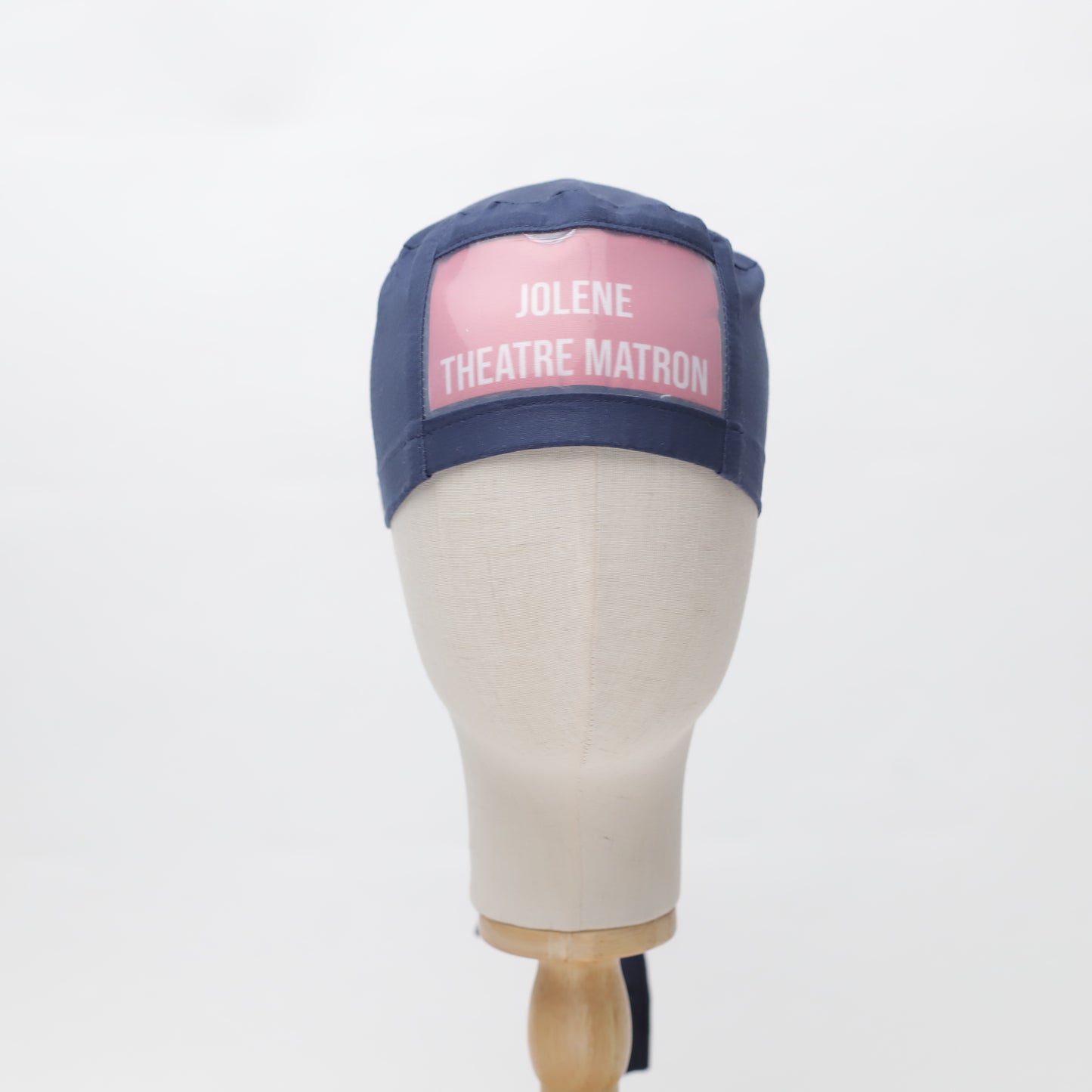 A mannequin head displays a navy Medicus Scrub Cap with a pink "Jolene Theatre Matron" patch, part of the ClearName collection in 22 colors.