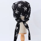 Back view of black scrub cap with white skull and crossbones pattern, showing tie detail