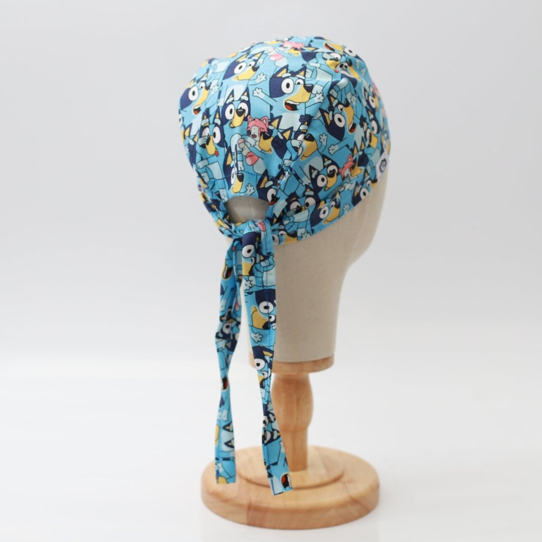 Blue Medicus Scrub Cap featuring a vibrant cartoon character pattern, tied at the back, displayed on a mannequin head.