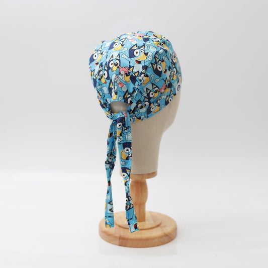 Blue Medicus Scrub Cap featuring a vibrant cartoon character pattern, tied at the back, displayed on a mannequin head.