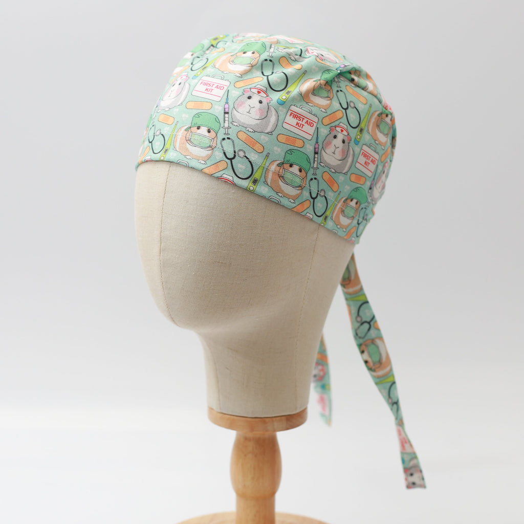 Medicus Scrub Cap with a cute guinea pig doctor and first aid pattern on a light green background, displayed on a mannequin head.