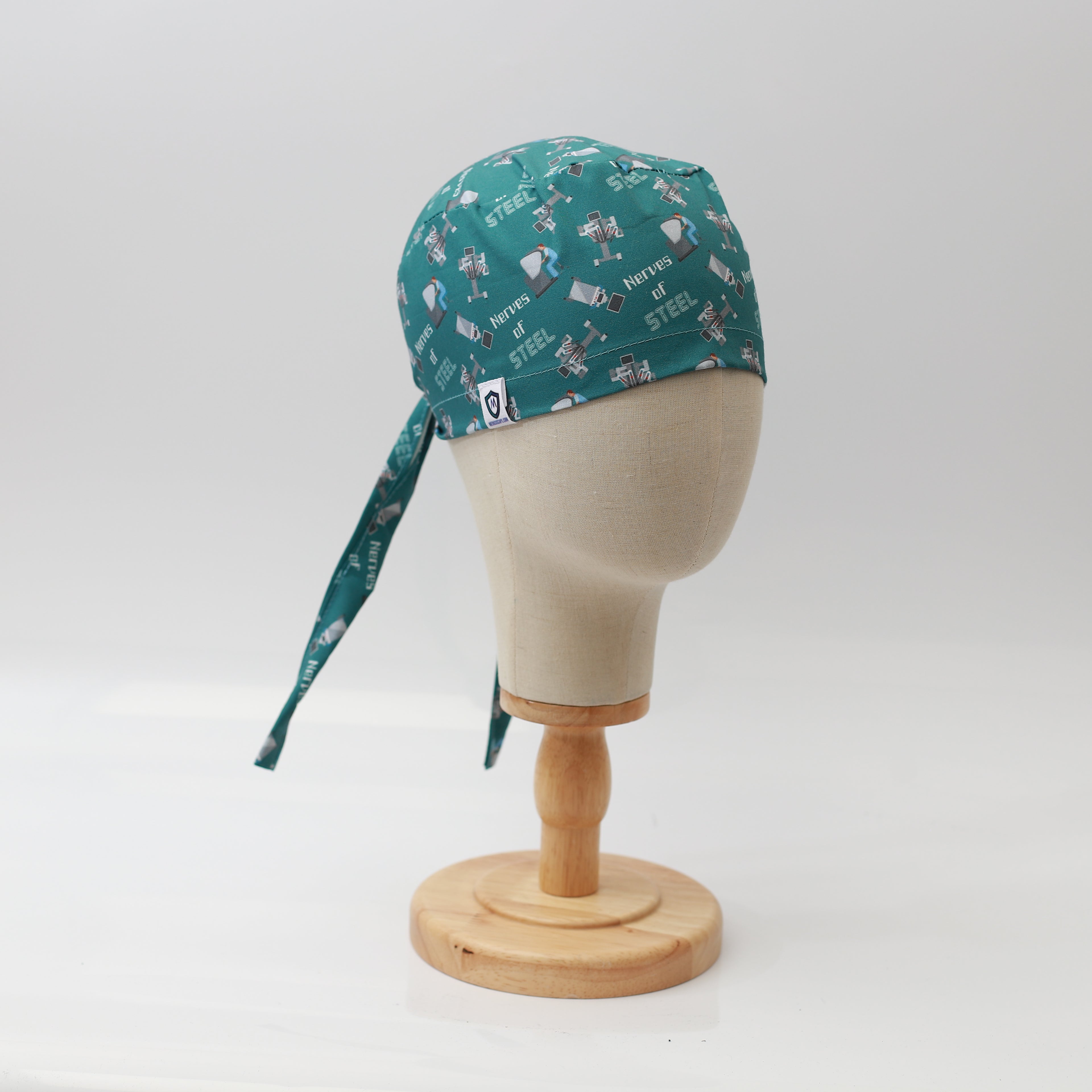 Mannequin head wearing Medicus Scrub Cap with "Nerves of Steel" robotic surgery green print, displayed on a wooden stand against a white background.