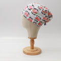 Mannequin head wearing Medicus Scrub Cap with pink lungs print and pun text, on a wooden stand against a white backdrop.