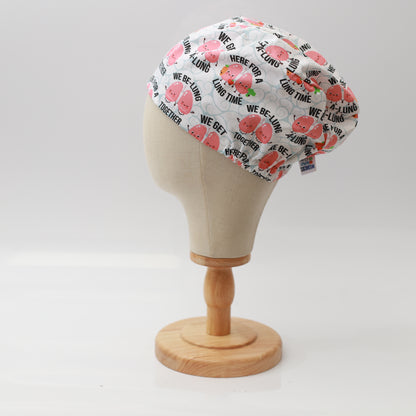 Mannequin head wearing Medicus Scrub Cap with pink lungs print and pun text, on a wooden stand against a white backdrop.