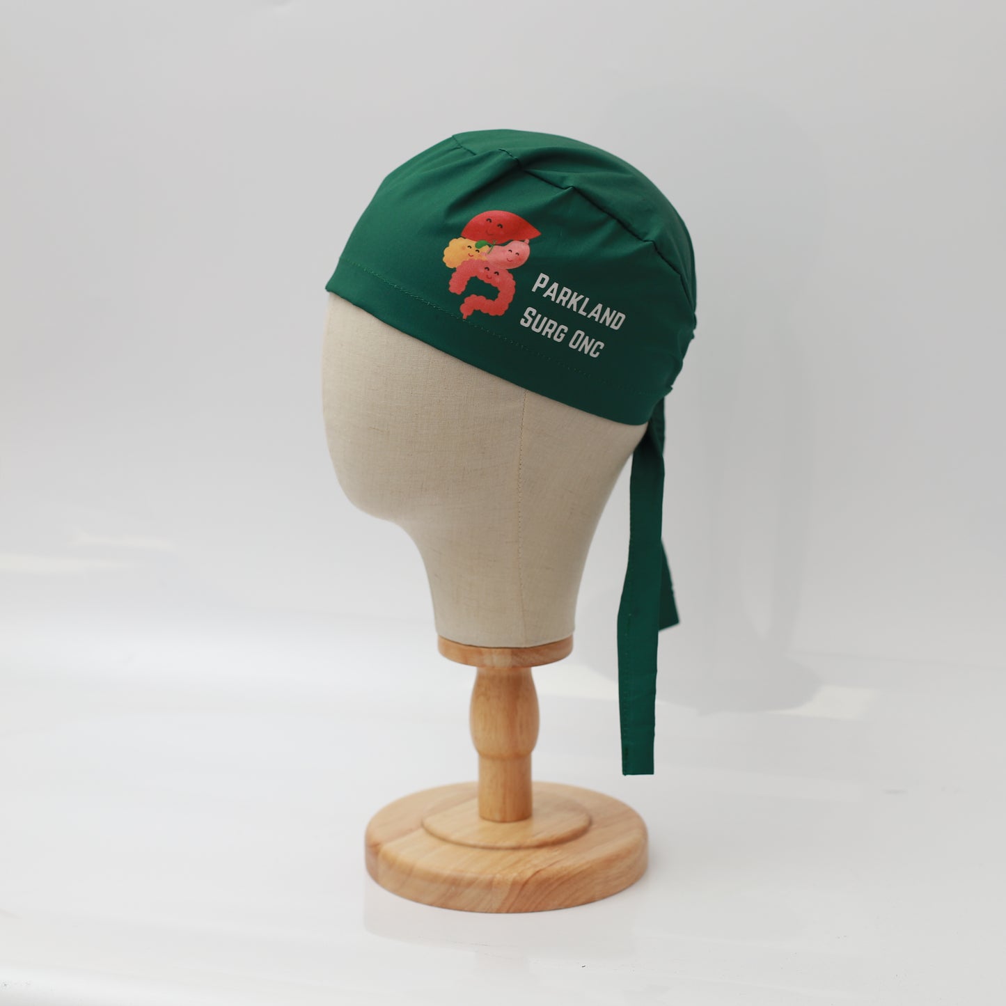 A Specific Custom Printed Placement Scrub Cap by Medicus Scrub Caps, featuring PARKLAND SURG ONC and a bear graphic on green fabric, displayed on a mannequin head.