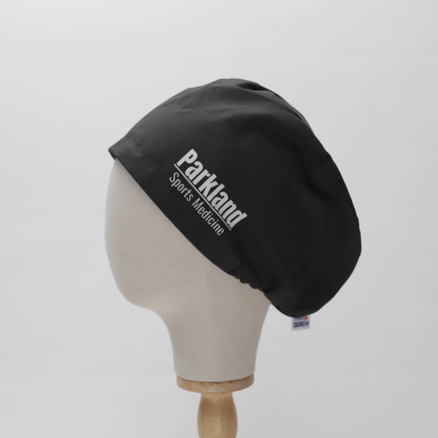 A black Parkland Sports Medicine embroidered scrub cap by Medicus Scrub Caps, displayed on a mannequin head, showcasing a custom-printed design and superior fit.