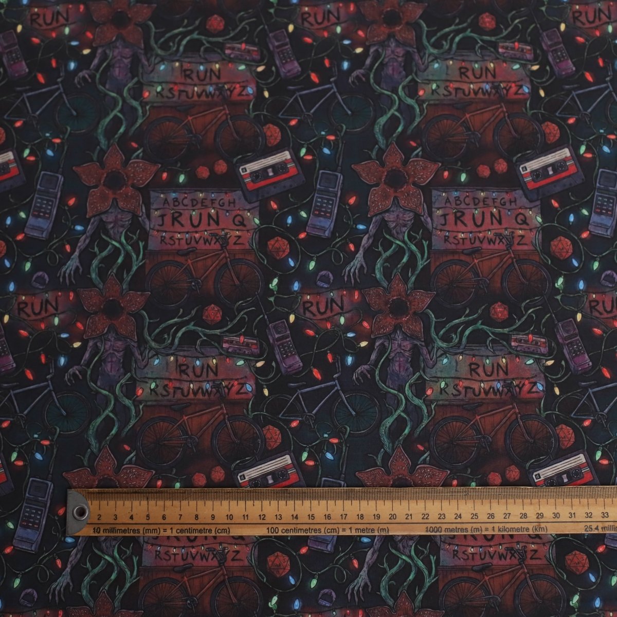 Textile with a dark background featuring colorful text, symbols, and a ruler for scale.