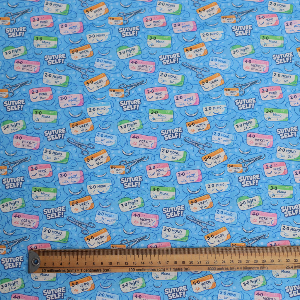 Patterned fabric with medical labels and tools on a blue background, ruler for scale.