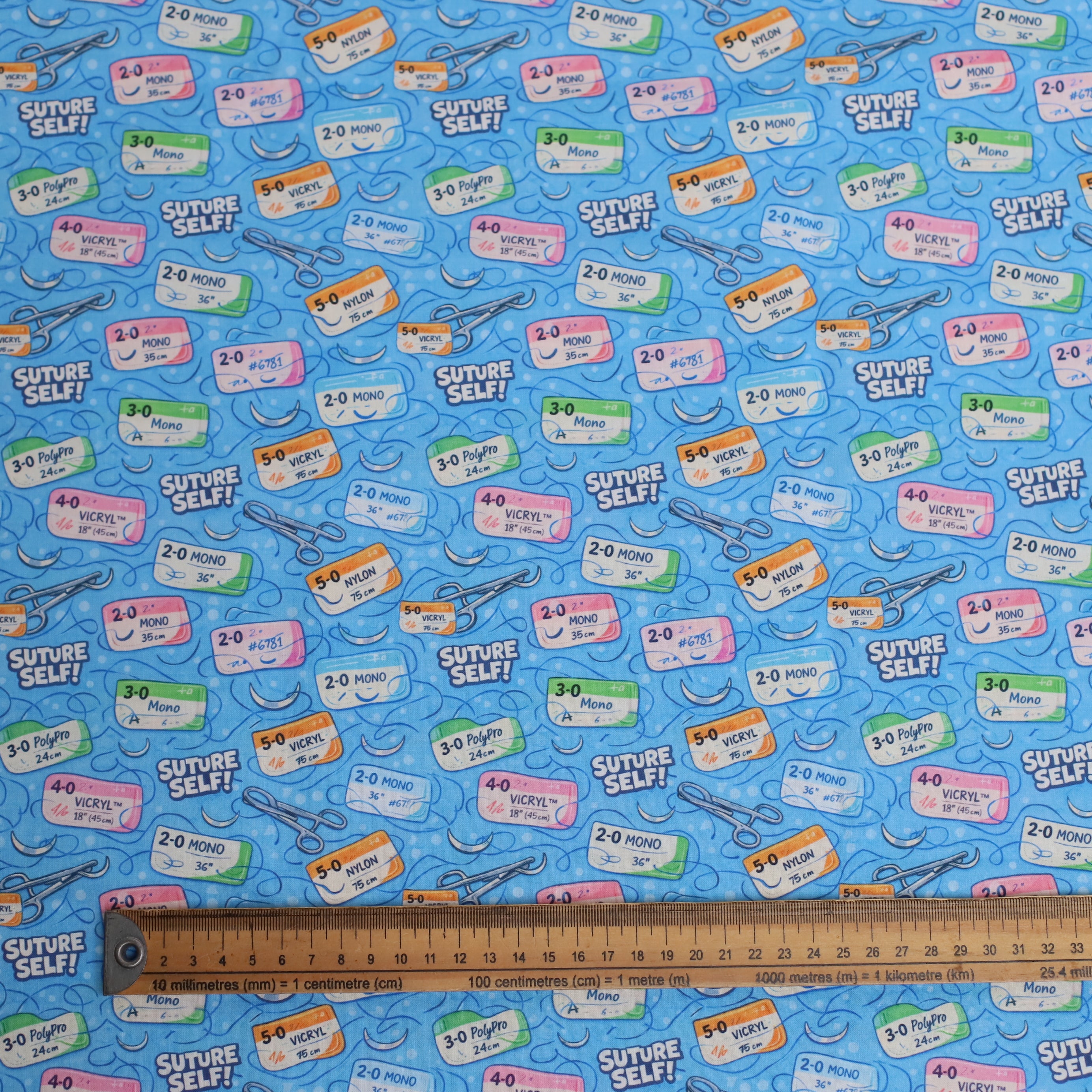 Patterned fabric with medical labels and tools on a blue background, ruler for scale.
