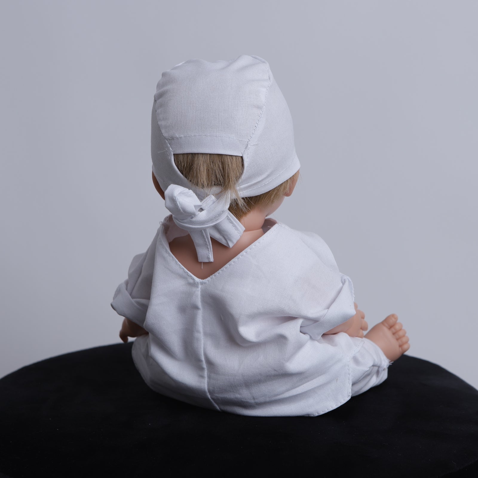 Doll wearing white scrubs and a matching Medicus Scrub Cap from @doll-scrubs-caps, sitting on a black surface.