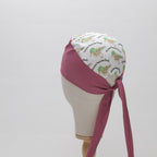 A mannequin head displays The Mullet scrub cap by Medicus Scrub Caps, featuring burgundy fabric and a patterned panel with ducks and text. Ties at the back.