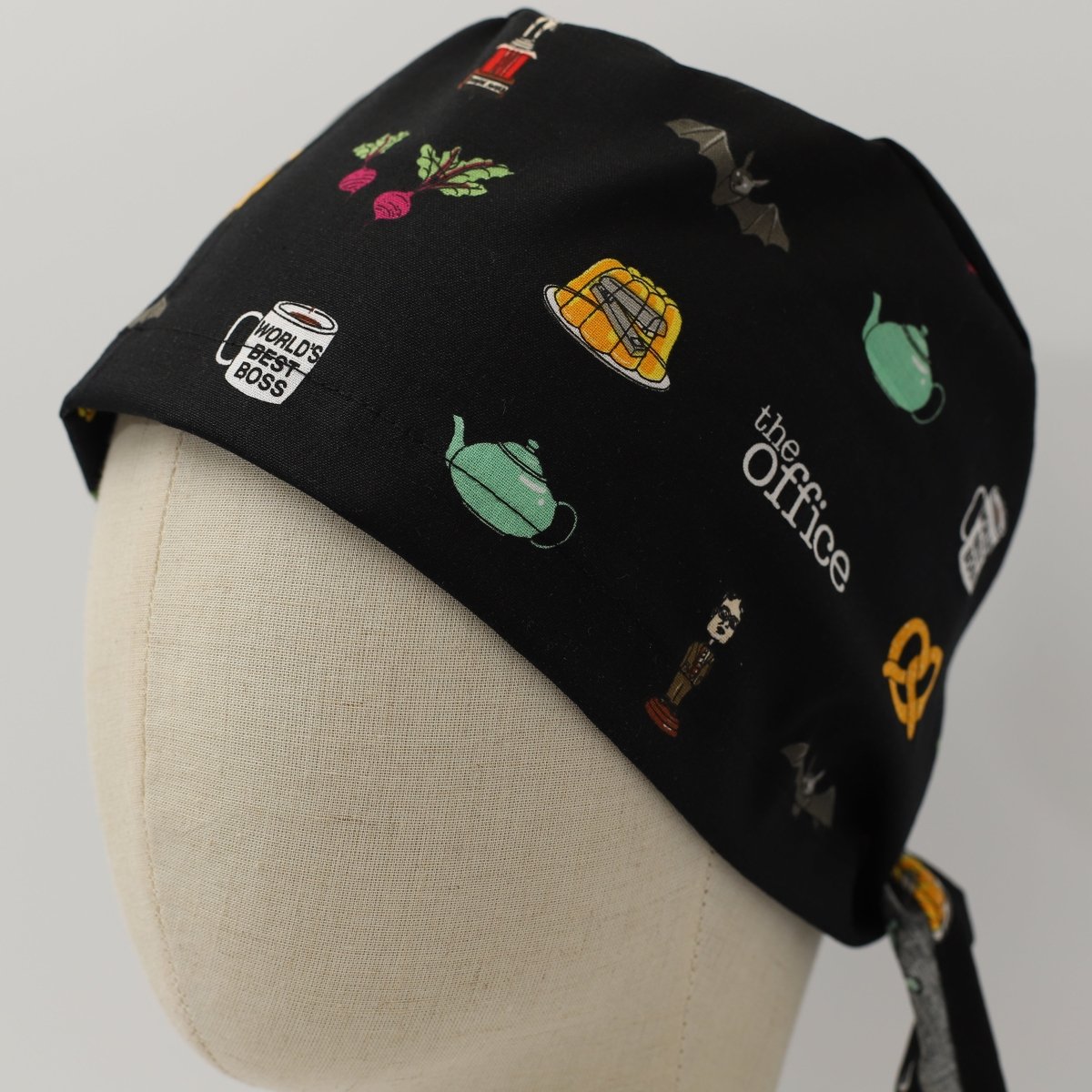 Black custom scrub cap featuring whimsical office-inspired icons including coffee mugs, teapots, pretzels, bats and beets. Handmade office icons scrub cap by Medicus Caps with playful design for medical professionals who love workplace humor.