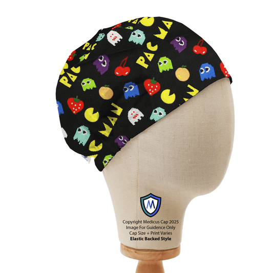 A mannequin head displays the Medicus Scrub Caps Games Pacman Retro Scrub Cap, featuring a colorful Pac-Man design with ghosts, fruit, and text on a black background.