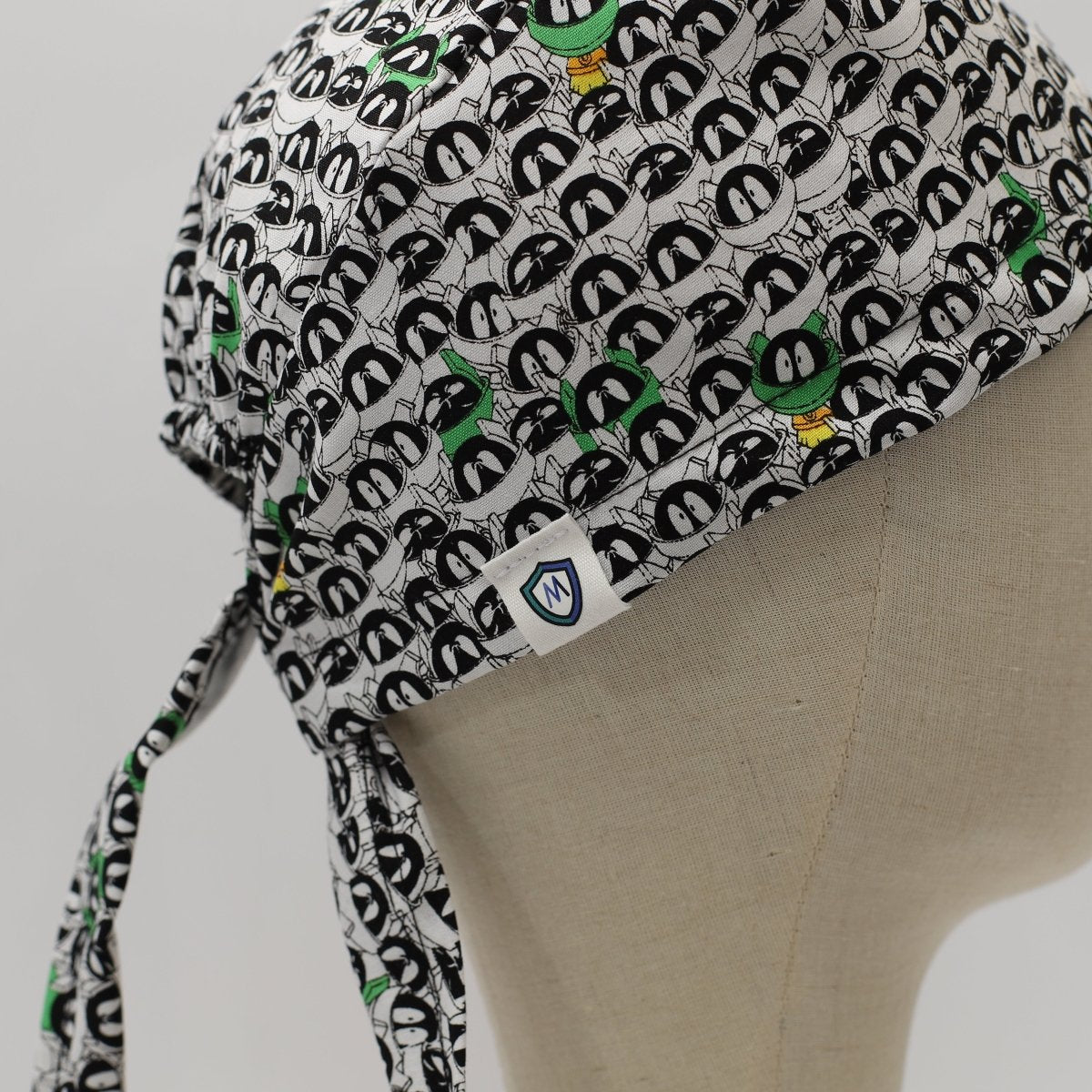 Custom scrub cap by Medicus Caps featuring black and white penguin face pattern with hints of green. Side view with long tie strap, handmade to order surgical cap.