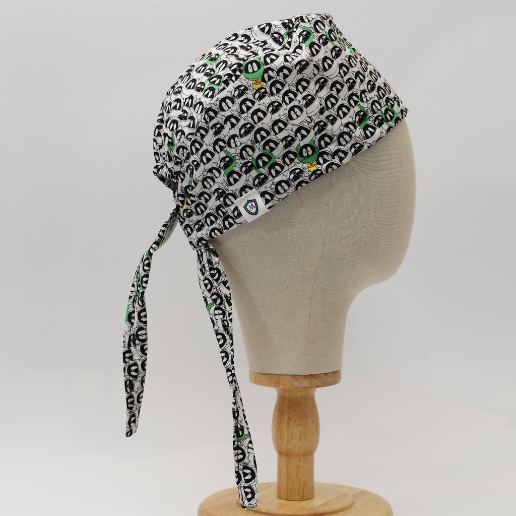 Custom scrub cap by Medicus Caps featuring black and white penguin face pattern with green accents. Side view with long ties; handmade surgical cap made to order.