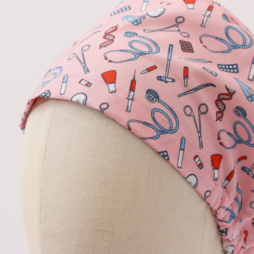 Custom pink scrub cap by Medicus Caps featuring illustrated medical tools like stethoscopes, syringes and scissors. Bouffant style surgical cap made to order.
