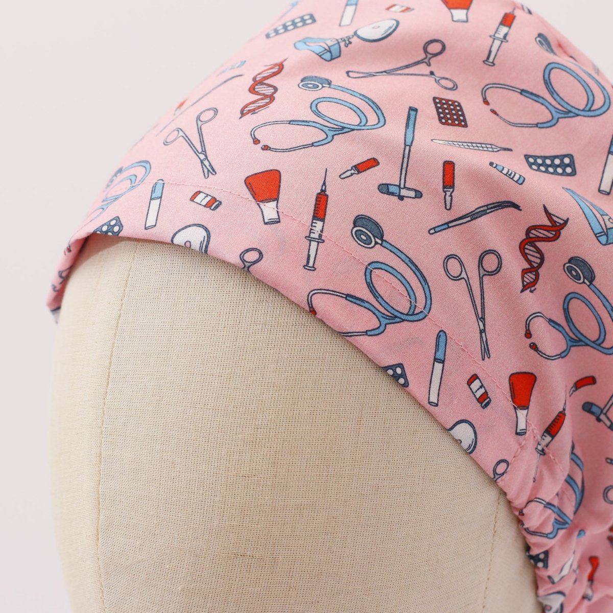 Custom pink scrub cap by Medicus Caps featuring illustrated medical tools like stethoscopes, syringes and scissors. Bouffant style surgical cap made to order.