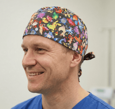 Colourful Pokemon character print scrub cap with tie-back closure worn by smiling medical professional