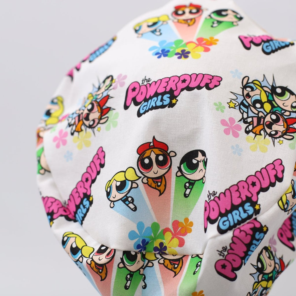 Custom white scrub cap featuring Powerpuff Girls cartoon print. Handmade by Medicus Caps with colorful characters and flowers, perfect for medical professionals seeking playful style.
