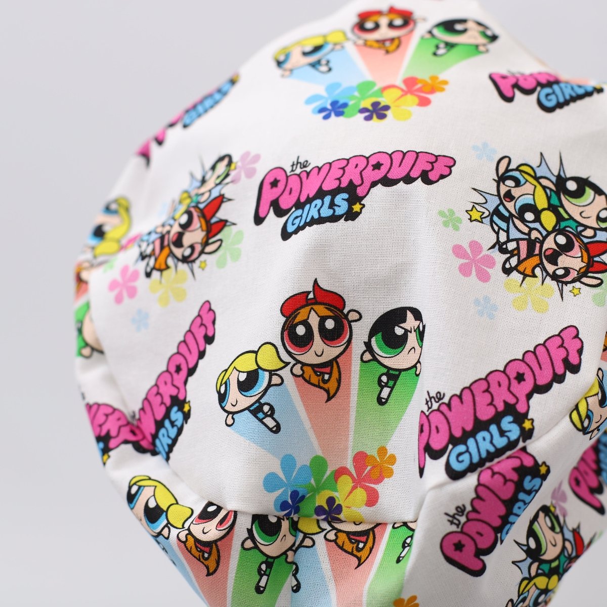 Custom white scrub cap featuring Powerpuff Girls cartoon print. Handmade by Medicus Caps with colorful characters and flowers, perfect for medical professionals seeking playful style.