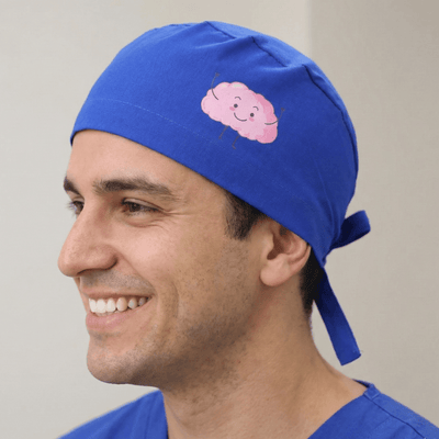 Royal blue scrub cap with pink smiling brain design and tie-back closure