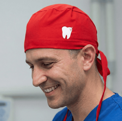Red scrub cap with white tooth design shown in side profile on smiling healthcare professional