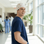 Male healthcare worker wearing watermelon patterned scrub cap, smiling in hospital hallway side profile view