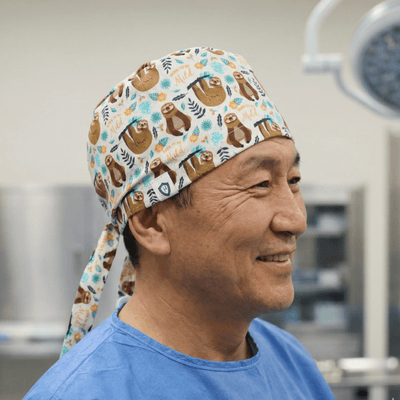 Brown sloth pattern scrub cap with turquoise accents worn by smiling healthcare professional