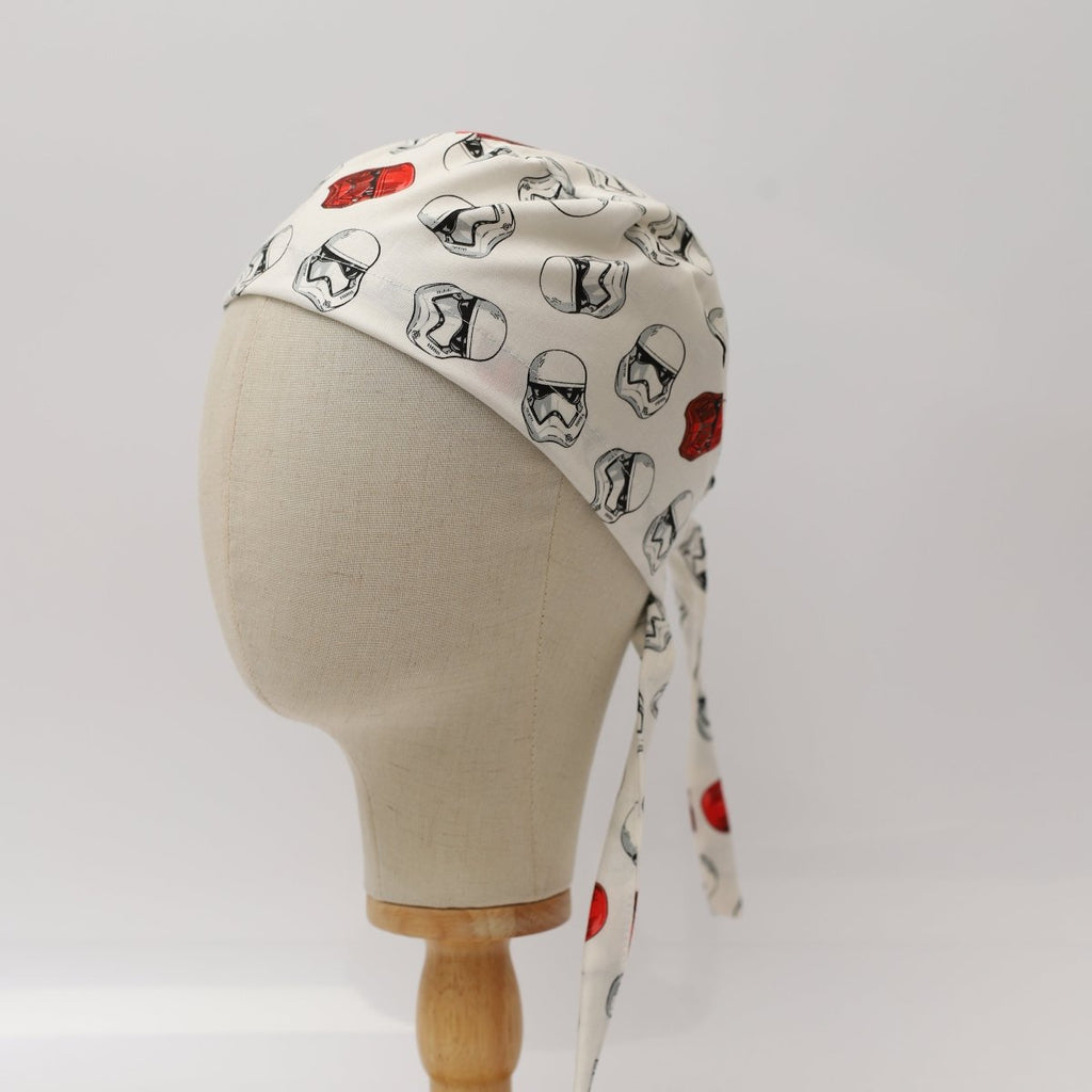 Custom white scrub cap by Medicus Caps featuring repeating black and red sci-fi helmet designs; back view on mannequin with long tie straps.