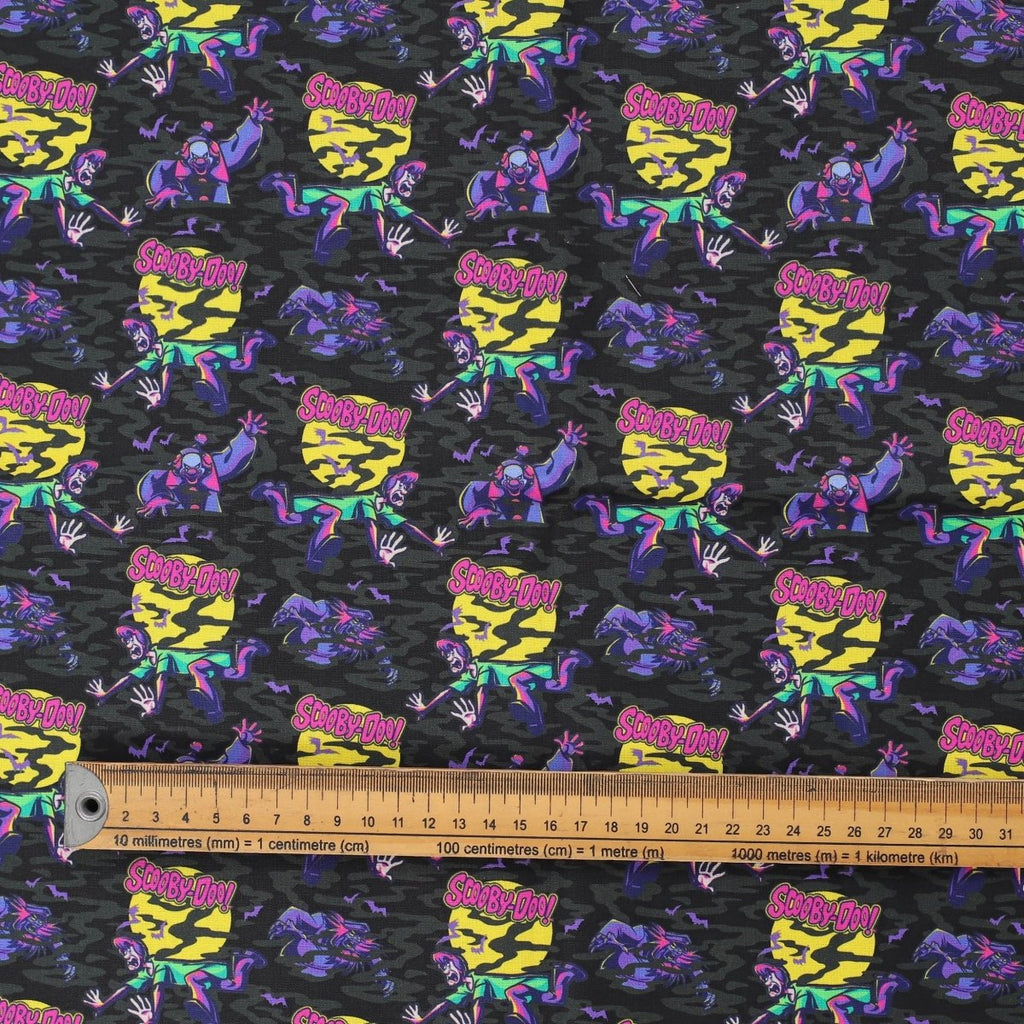 Close-up of Scooby-Doo purple scrub cap fabric featuring characters and ruler for scale.