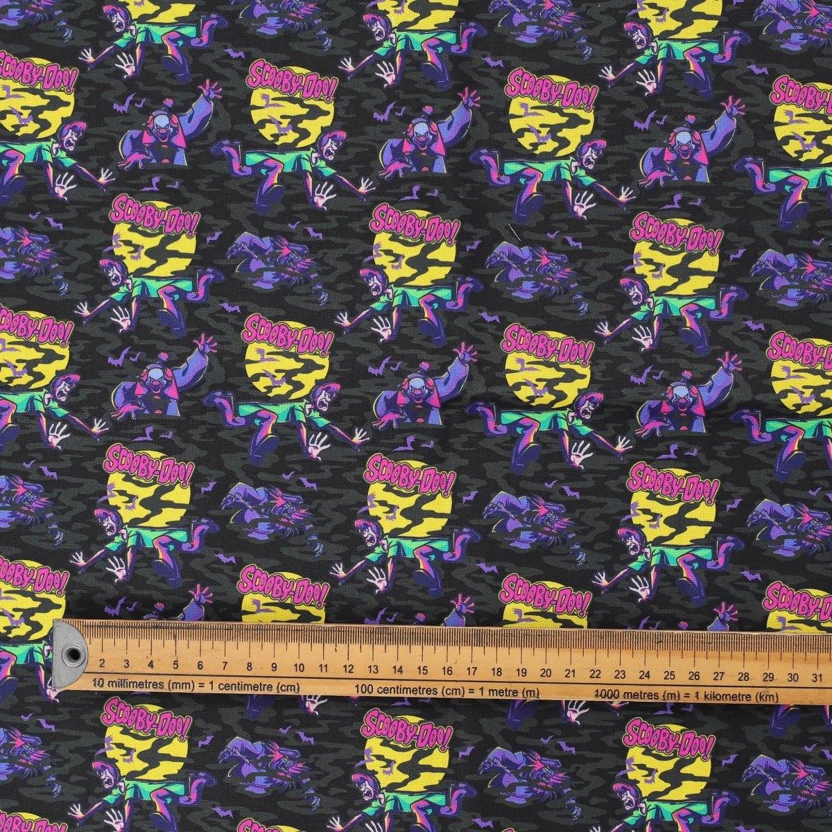 Close-up of Scooby-Doo purple scrub cap fabric featuring characters and ruler for scale.