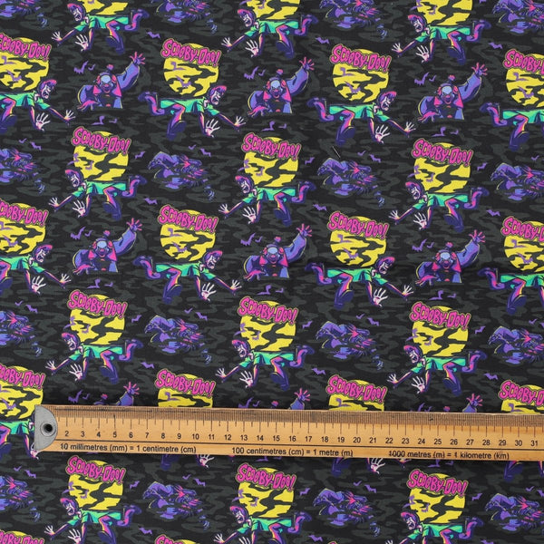 Close-up of Scooby-Doo purple scrub cap fabric featuring characters and ruler for scale.