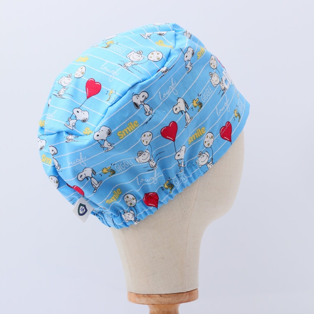 Blue bouffant scrub cap featuring Snoopy cartoon characters, red hearts and 'smile' text. Handmade custom scrub cap by Medicus Caps with adjustable fit.
