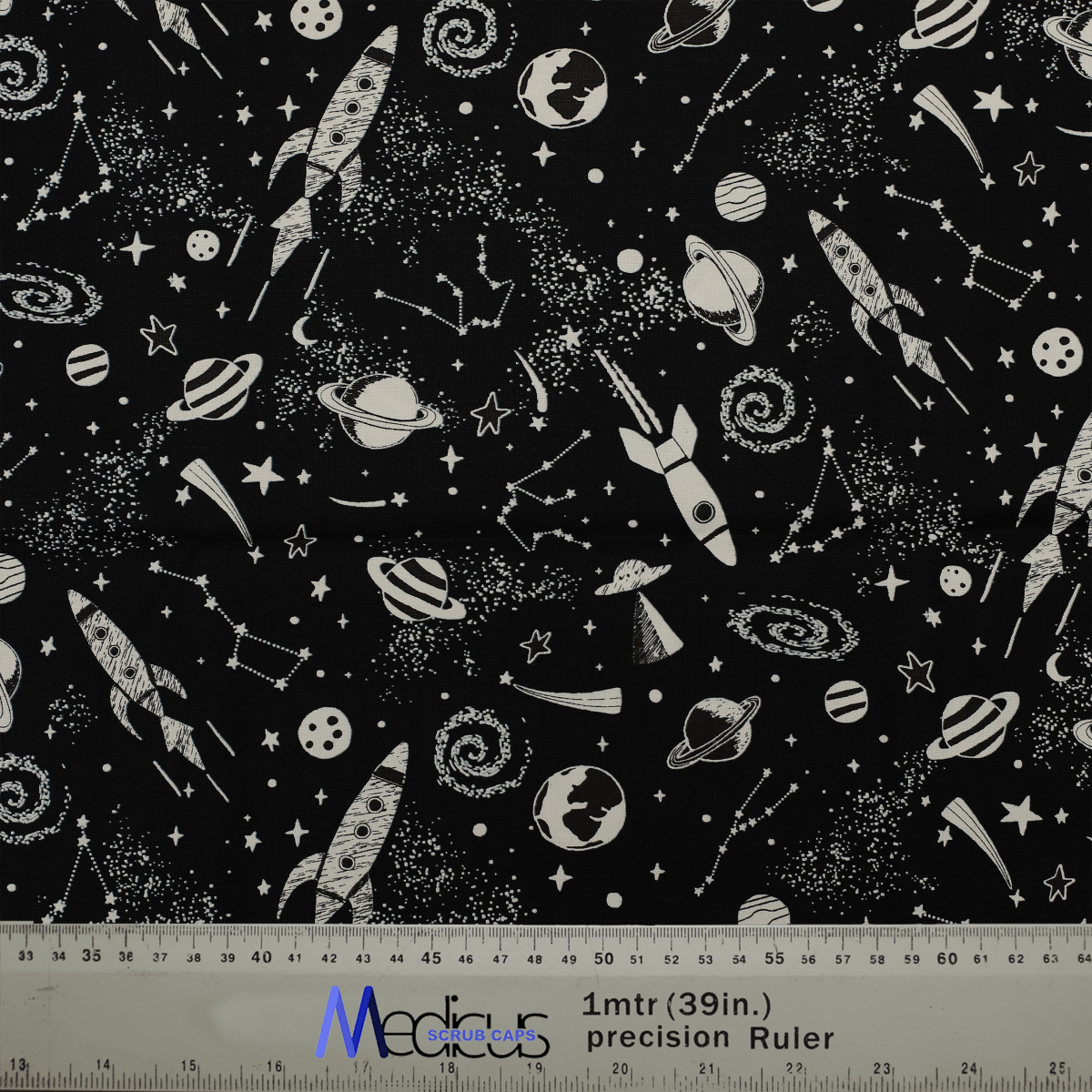 Close-up of glow-in-the-dark rockets and space-themed fabric for Medicus Scrub Caps, with a ruler for measurement reference.