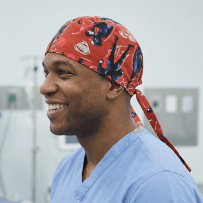 Red Superman comic print scrub cap with tie-back closure worn by smiling healthcare worker