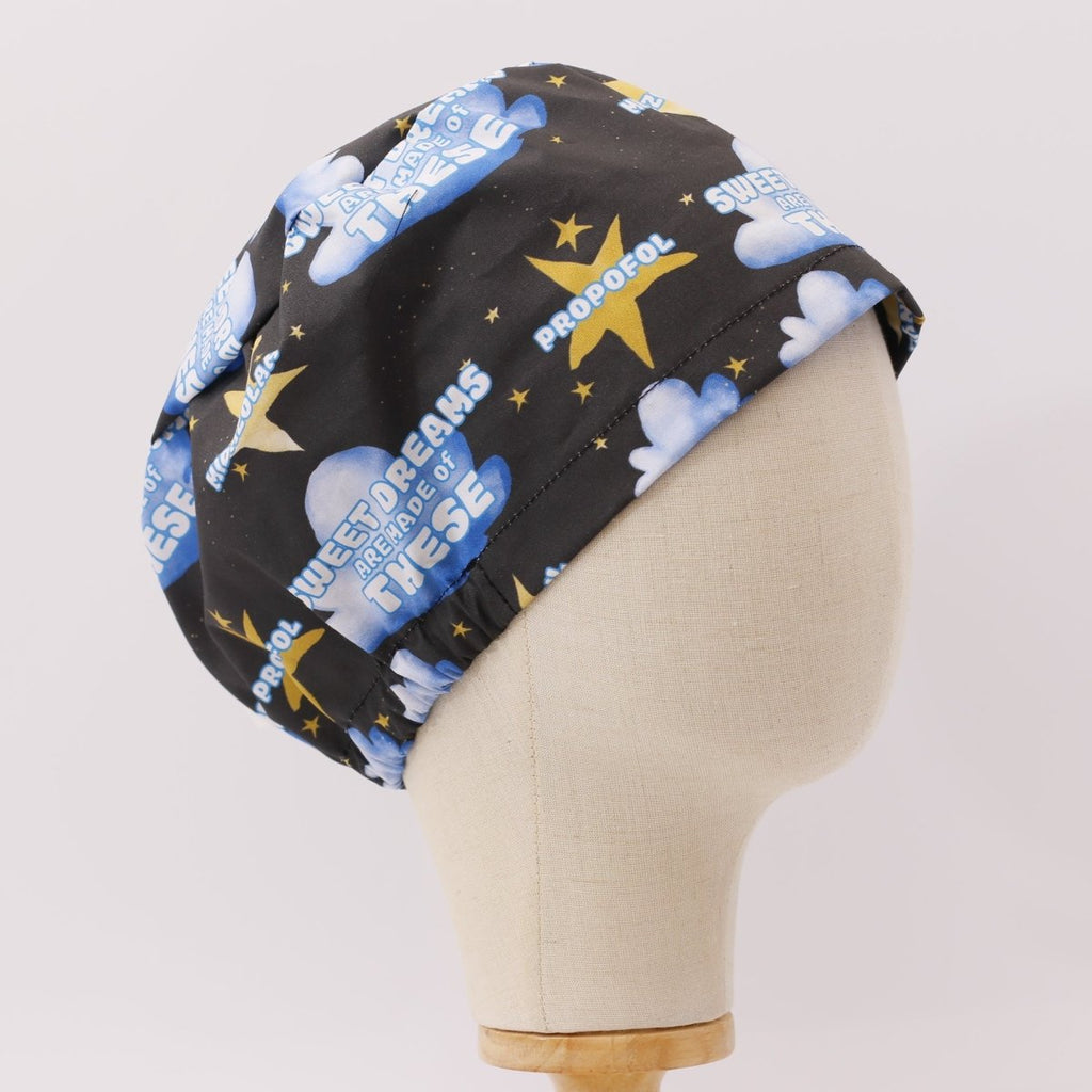 Custom black scrub cap by Medicus Caps featuring the phrase 'Sweet dreams are made of propofol' with blue clouds, stars and syringes. Handmade surgical cap for anesthetists.