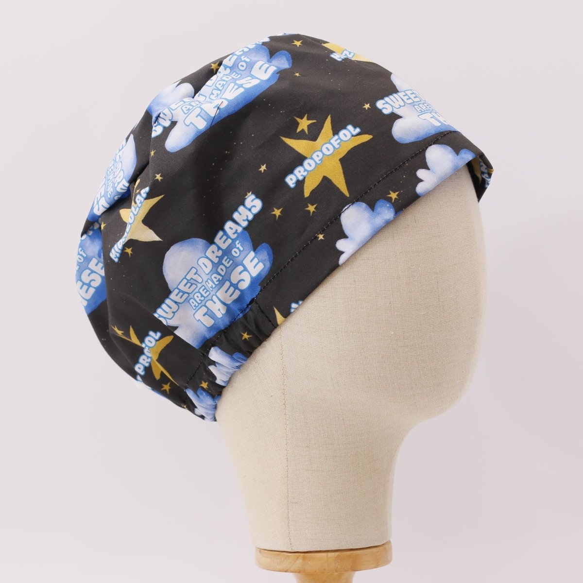Custom black scrub cap by Medicus Caps featuring the phrase 'Sweet dreams are made of propofol' with blue clouds, stars and syringes. Handmade surgical cap for anesthetists.